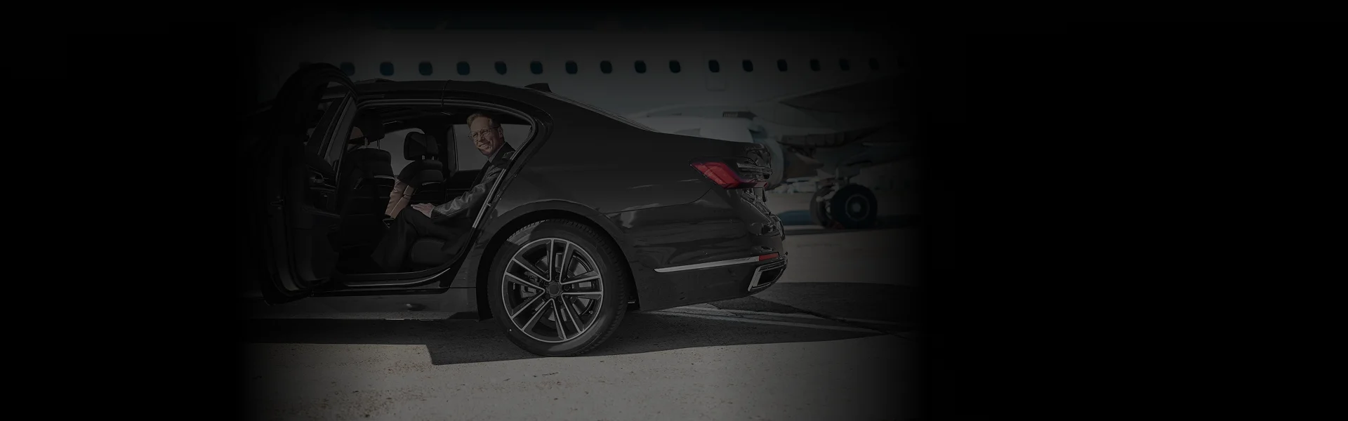 Business traveler seated inside a luxury black car on the tarmac beside a private jet, promoting Philadelphia Airport Car Service with a low side view for an exclusive, executive look.